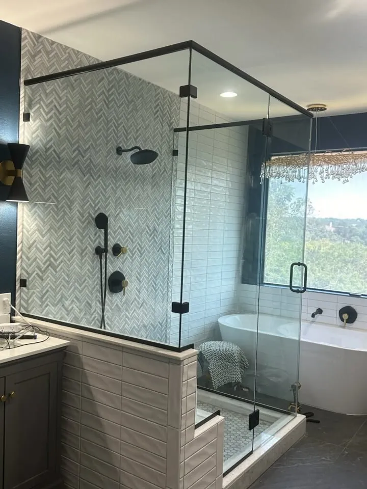 Frameless glass shower enclosure with herringbone tile walls and matte black hardware, installed in a Georgetown, TX bathroom